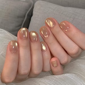 Peut inclure: Gros plan sur une main avec des ongles vernis. Les ongles sont peints d'une couleur or chatoyante, créant un effet réfléchissant. La manucure a une finition brillante, améliorant l'esthétique générale. Les ongles sont de forme ovale.