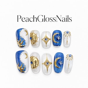 Peut inclure: Un ensemble de dix faux ongles étiquetés PeachGlossNails, présentant un thème céleste avec des fonds bleu et blanc scintillants, des motifs de soleil et de lune en métal doré, et de petits strass bleus et transparents disposés en motifs.