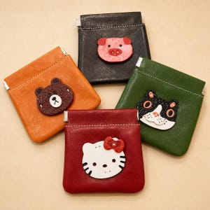 May include: Four square leather coin pouches in black, orange, green, and red. Each pouch features a stitched animal face appliqué: a pink pig, a brown bear, a black and white cat, and a white cat with a red bow. Each has a metal frame closure.