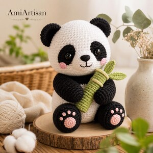May include: A crocheted panda toy with a white head and body, black ears, arms, and legs. The panda has black eye patches, pink cheeks, and black safety eyes. It holds a green crocheted bamboo stalk with two leaves. The feet feature pink paw pads.
