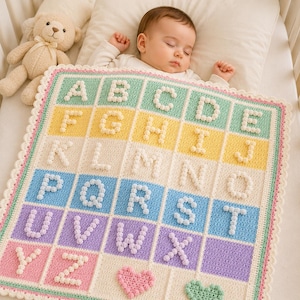 May include: A colorful, handmade baby blanket with the alphabet in a grid pattern. Each letter is made of white bobbles, set against pastel squares of green, yellow, blue, purple, and pink. A teddy bear is in the background.