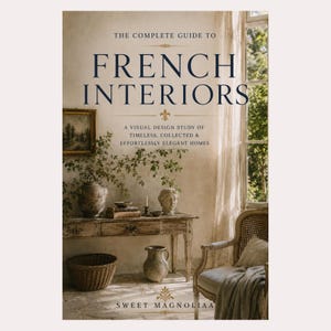May include: A hardcover book titled The Complete Guide to French Interiors: A Visual Design Study of Timeless, Collected & Effortlessly Elegant Homes by Sweet Magnoliaa. The cover features a rustic wooden console table, a wicker basket, and a chair.