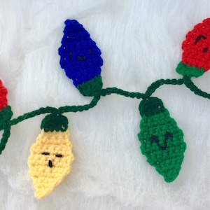 May include: A string of crocheted Christmas lights with different colored bulbs and happy faces. The lights are red, blue, green, and yellow.
