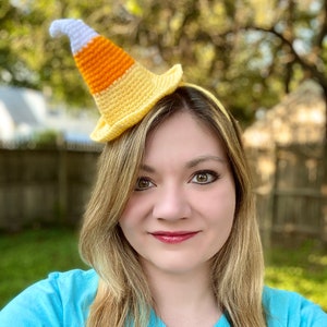 Puede incluir: Una mujer lleva una diadema de maíz dulce de crochet amarillo y naranja. La diadema tiene forma de cono y tiene una punta blanca.