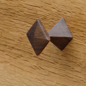 May include: A dark brown wooden drawer pull with a diamond shape. The pull is attached to a wooden surface.