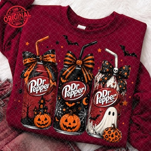 Peut inclure: Un t-shirt à manches longues bordeaux avec un motif de trois canettes de Dr Pepper décorées sur le thème d'Halloween. Chaque canette comporte une paille, un nœud à motifs et des illustrations de citrouilles, d'un manoir, de chauves-souris et d'un fantôme.