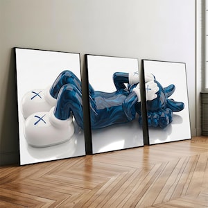 May include: Three framed art prints featuring a stylized blue figure with white gloves and boots. The figure is in a relaxed pose, with its hands covering its eyes. The prints are displayed on a wall above a wooden floor.