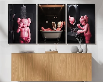 May include: A triptych of framed art prints featuring a pink cartoon figure in a bathroom setting. One print shows the figure under a shower, another in a bathtub reading, and the third at a sink. The background is black, and the art is displayed above a wooden cabinet.