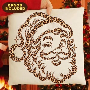 Op de afbeelding: Een wit vierkant kussen met een afbeelding van de Kerstman in een bruin en zwart luipaardpatroon. Het ontwerp bevat vierpuntige sterren en de tekst 2 PNGS INCLUDED in de linkerbovenhoek van de afbeelding.