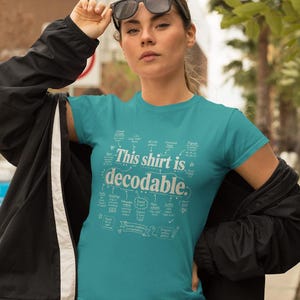 May include: A teal short-sleeved t-shirt featuring white text and diagrams. The central text reads, "This shirt is decodable." Surrounding the text are various linguistic labels and arrows pointing to specific terms like closed syllable, digraph, and suffix.