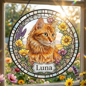 May include: A circular stained glass suncatcher featuring a detailed illustration of an orange tabby cat surrounded by colourful flowers including yellow daisies and purple lavender. A white plaque at the bottom displays the name Luna in black text.