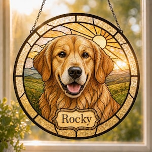 May include: A circular stained glass suncatcher featuring a golden retriever portrait with a smiling expression. The background depicts a sunburst over a landscape. A decorative plaque at the bottom contains the name Rocky in black lettering.