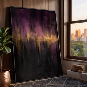 May include: Abstract art print in a black frame. The artwork features a blend of purple, gold, and black vertical brushstrokes. The painting leans against a wooden wall near a window with a city view.