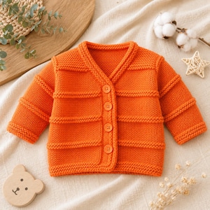 Könnte beinhalten: Eine leuchtend orangefarbene, langärmelige Strickjacke mit V-Ausschnitt, einer Knopfleiste vorne mit vier passenden orangefarbenen Knöpfen sowie horizontalen, strukturierten Rippenmustern an Körper und Ärmeln mit gerippten Bündchen.