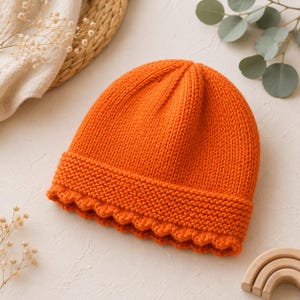 May include: A bright orange knitted beanie featuring a textured garter stitch cuff at the base and a smooth stockinette stitch pattern on the crown. The hat is constructed with a visible seam running from the top to the folded brim edge.