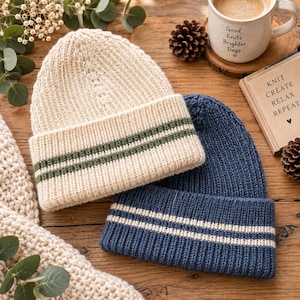 Puede incluir: Un gorro de punto color crema con dos rayas verde oscuro en el dobladillo y un gorro de punto azul marino con dos rayas blancas en el dobladillo. Ambos gorros presentan una textura acanalada y un diseño de borde doblado, presentados como un par.