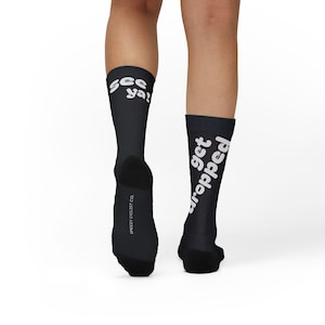 May include: Black athletic socks with white text reading "see ya!" and "get dropped." The socks also feature the text "SPEEDY CYCLIST CO." on the side. These socks are designed for cycling and are suitable for various sports.