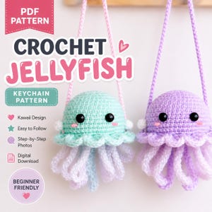 May include: A digital PDF pattern for a crochet jellyfish keychain. The image displays two finished jellyfish toys, one mint green and one lavender, each with black eyes, pink cheeks, and hanging tentacles, suspended by light pink yarn loops.