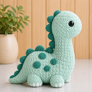 Puede incluir: Un dinosaurio de ganchillo verde claro hecho a mano con manchas y espinas de color verde oscuro. El dinosaurio tiene una cabeza redonda con un ojo negro grande y pies blancos. Este peluche es un artículo lindo.