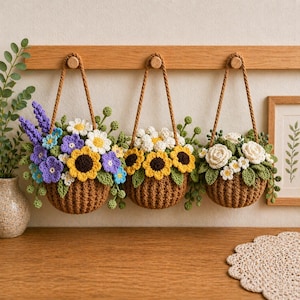 May include: Three crochet baskets filled with colourful flowers hang from a wooden beam. The baskets are brown, with rope handles. The flowers include sunflowers, daisies, and roses in shades of yellow, white, and purple, with green leaves.
