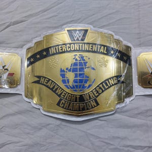 May include: A gold-colored Intercontinental Heavyweight Wrestling Champion belt. The belt features the WWE logo, the words "Intercontinental" and "Heavyweight Wrestling Champion", and a blue and gold globe design.