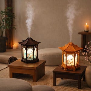 Puede incluir: Dos difusores de aceites esenciales de madera decorativos, estilo pagoda, con un diseño floral claro en los paneles interiores. Los difusores están sobre pequeñas mesas de madera, con vapor saliendo de la parte superior. Una vela y plantas en el fondo.