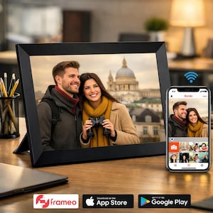 Puede incluir: Un marco de fotos digital negro muestra una foto de una pareja sonriente. Un smartphone muestra la misma imagen. El marco y el teléfono están sobre una superficie de madera. El marco tiene la palabra "frameo" en la parte inferior.