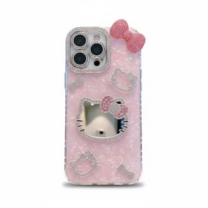 May include: Pink phone case with a Hello Kitty design. The case features a bow, Hello Kitty face, and other decorative elements, all encrusted with rhinestones. The camera lens is surrounded by a silver rhinestone border.