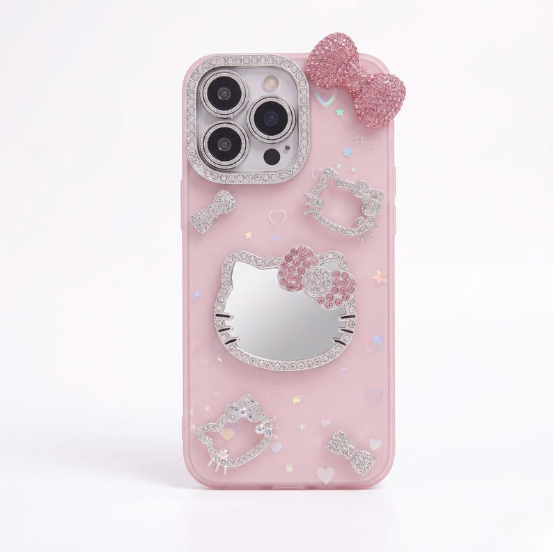 May include: Pink phone case with a Hello Kitty design. The case features a bow, a Hello Kitty face, and other decorative elements, all adorned with sparkling rhinestones. The camera area is also embellished with rhinestones.