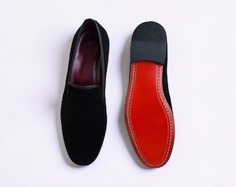 Black suede loafers feature a distinctive red sole, characteristic of Christian Louboutin luxury footwear