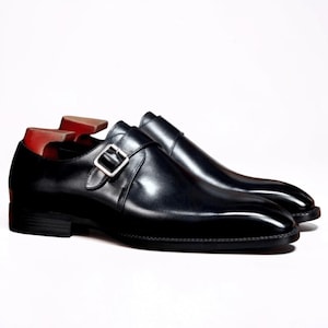 Könnte beinhalten: Ein Paar schwarze Lederschuhe mit einem silbernen Schnallenverschluss. Die Schuhe haben ein glänzendes Aussehen und stehen vor einem weißen Hintergrund. Das Innere des Schuhs ist rot.