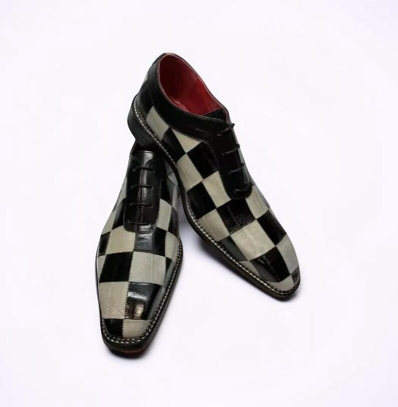 May include: A pair of men's dress shoes with a black and gray checkerboard pattern. The shoes have black laces, a black toe cap, and a red interior. The shoes are made of leather and have a classic Oxford style.