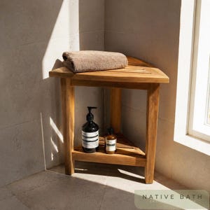 Puede incluir: Un banco de ducha esquinero de madera con una toalla marrón doblada encima. Dos botellas oscuras se encuentran en el estante inferior. El banco está en un baño con ventana y paredes alicatadas. El texto "NATIVE BATH" está en la parte inferior.