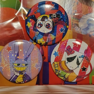 May include: Three circular pin-back buttons featuring colorful anime-style character illustrations with a holographic glitter finish. The designs include a jester-like figure, a purple rabbit character, and a masked figure with a red and white striped background.