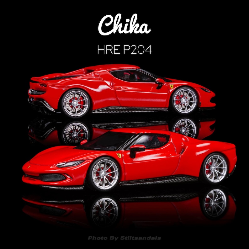 May include: Two red toy cars, a Ferrari model, are displayed on a black surface. The cars have silver wheels and are reflected in the glossy surface. The text "Chika" and "HRE P204" are visible.