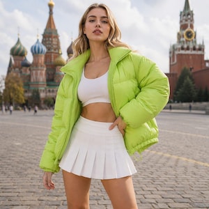 May include: A woman wearing a bright green puffer jacket, a white crop top, and a white pleated skirt. The jacket has a high collar and a drawstring at the hem. The outfit is set against a backdrop of a historic building.