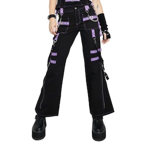 May include: Black pants with purple accents, featuring multiple straps, chains, and zippers. The pants have a wide-leg design and are paired with platform shoes. The overall style is edgy and alternative.