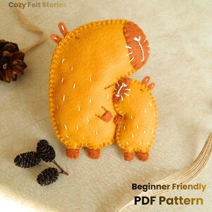 May include: A handmade felt animal in shades of orange and brown, with white stitching details. The felt animal has a larger body and a smaller body attached, with the text "Beginner Friendly PDF Pattern".