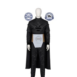 May include: A black costume set featuring a long-sleeved top with white stitching, a high collar, and a cape. The outfit includes matching black trousers and a light grey waist sash with a tan border. The ensemble is displayed on a mannequin.