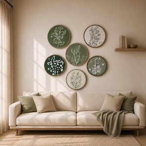 May include: A living room scene featuring a beige sofa with olive green and tan pillows and a matching throw blanket. Above the sofa, six round botanical art pieces with wooden frames are displayed on the wall. The art pieces feature various plant illustrations.