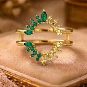 May include: A gold ring with a double band design. The ring features a half-circle of emerald green and yellow gemstones. The gemstones are arranged in a sunburst pattern. The ring's design is eye-catching.