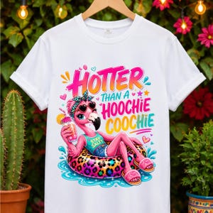 May include: White t-shirt with a colorful graphic of a flamingo wearing sunglasses and a headband, lounging on a leopard-print float. The text reads "Hotter Than a Hoochie Coochie". The flamingo is holding a drink.