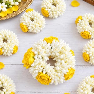 May include: A collection of circular floral garlands crafted from small white jasmine buds and accented with vibrant yellow roses. Each wreath features a dense, textured arrangement of white petals contrasted by bright yellow rose blossoms.
