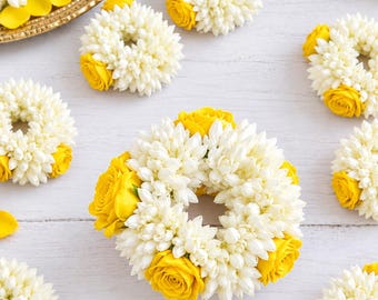 May include: A collection of circular floral garlands crafted from small white jasmine buds and accented with vibrant yellow roses. Each wreath features a dense, textured arrangement of white petals contrasted by bright yellow rose blossoms.