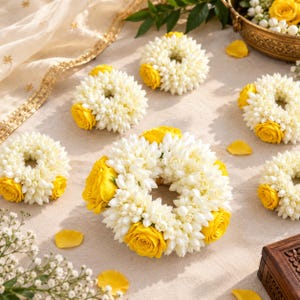 May include: Several circular floral garlands crafted from small white jasmine-like blossoms and vibrant yellow roses. The arrangements are arranged in a cluster, featuring dense white petals interspersed with bright yellow rose heads.