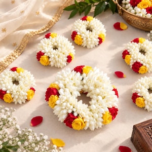 May include: A collection of circular floral garlands crafted from white jasmine buds, accented with vibrant red and yellow rose blossoms. These decorative wreaths are arranged in a cluster, featuring dense, layered petals and a fragrant, natural aesthetic.