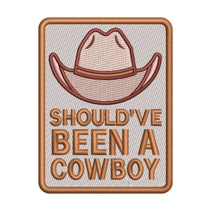 May include: Embroidered patch with a cowboy hat design. The patch features a light brown cowboy hat with a dark brown outline and trim. The text "SHOULD'VE BEEN A COWBOY" is embroidered in dark brown block letters.