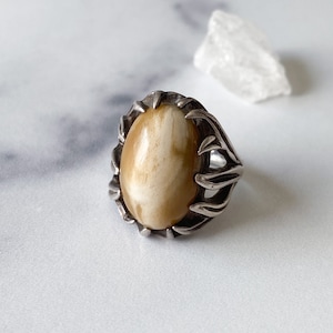 May include: A silver ring with a large oval-shaped ivory stone set in a detailed, branch-like design.