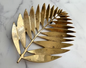 May include: A decorative brass leaf, featuring a detailed design with individual leaf segments. The golden-toned metal has a slightly aged appearance, adding to its vintage charm. The leaf is approximately 10 inches long.