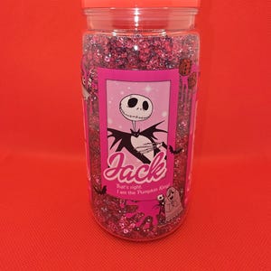 K&ouml;nnte beinhalten: Ein klares Glas mit rosa Glitzer und einem rosa Deckel. Das Glas hat ein rosa Etikett mit einer Illustration von Jack Skellington. Auf dem Etikett steht "Jack" und "That's right, I am the Pumpkin King!"